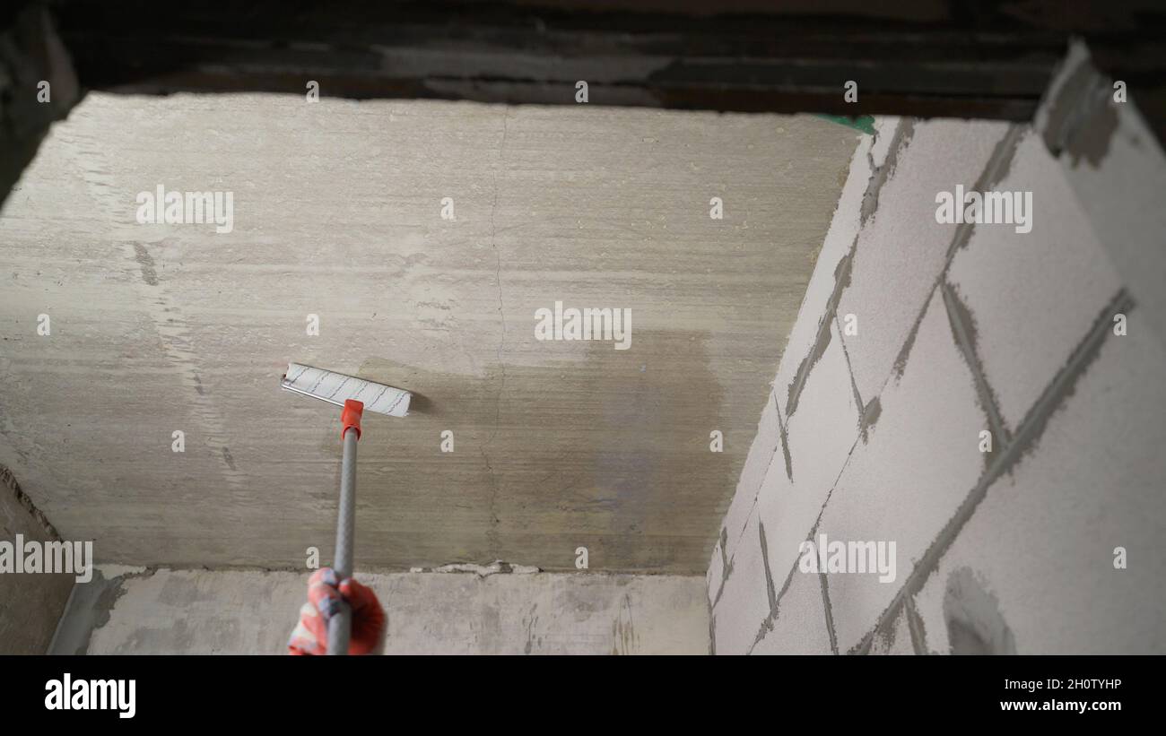 Innesco del soffitto con un rullo. Primer di lavoro con un rullo per verniciatura a soffitto. Primo piano del processo di adescamento del calcestruzzo. Foto Stock