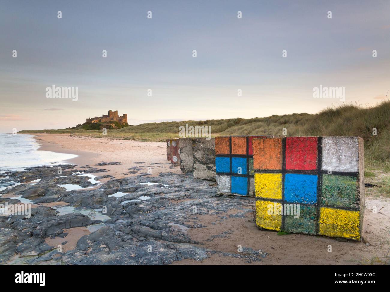 Castello e spiaggia di Bambburgh con le difese marine dipinte di dadi e rubix cubo al crepuscolo con un cielo limpido, sulla costa Northumberland dell'Inghilterra nord-orientale Foto Stock