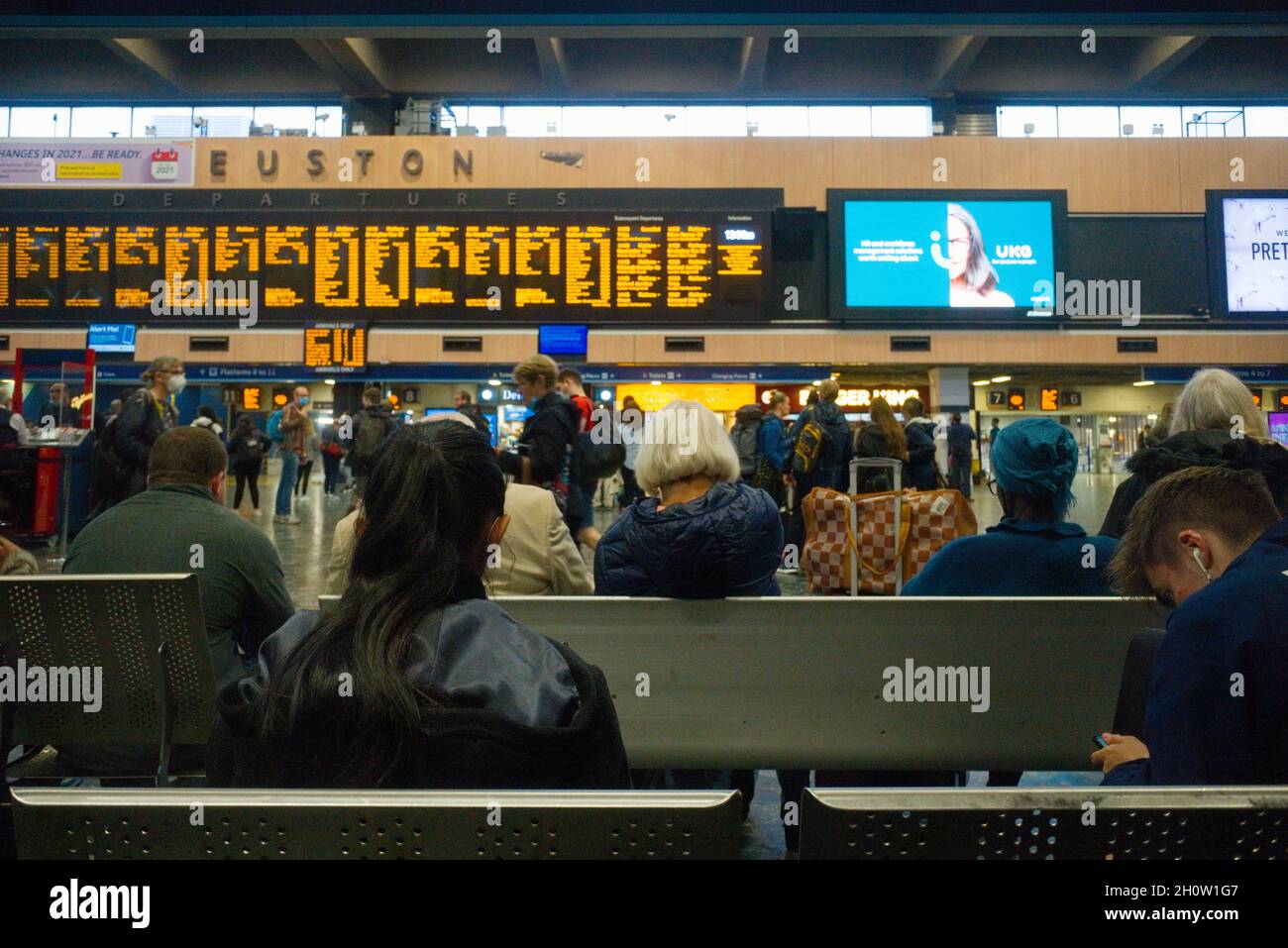 Stazione di Euston in attesa di treni che guardino le partenze durante gli orari più tardi, quindi alcune persone che indossano le coperture facciali Foto Stock