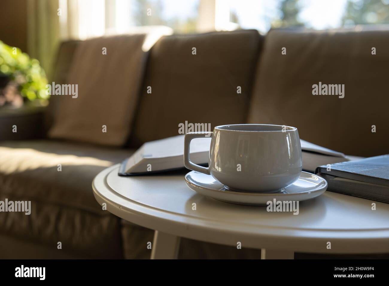 caffè su un piattino su un tavolo da caffè bianco rotondo con libro aperto, bibbia, di fronte ad un divano di pelle Foto Stock
