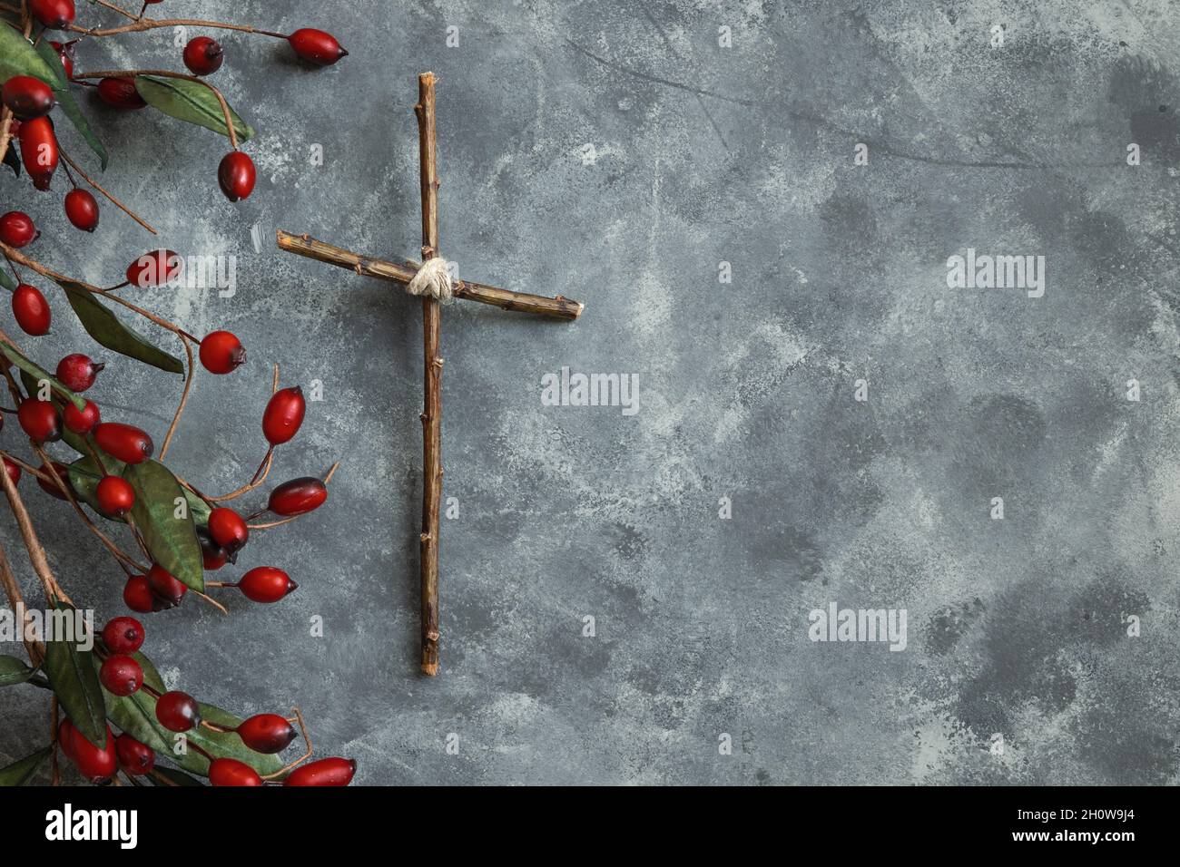 Semplice croce di legno con bordo di bacca di Natale su sfondo grigio con spazio copia Foto Stock