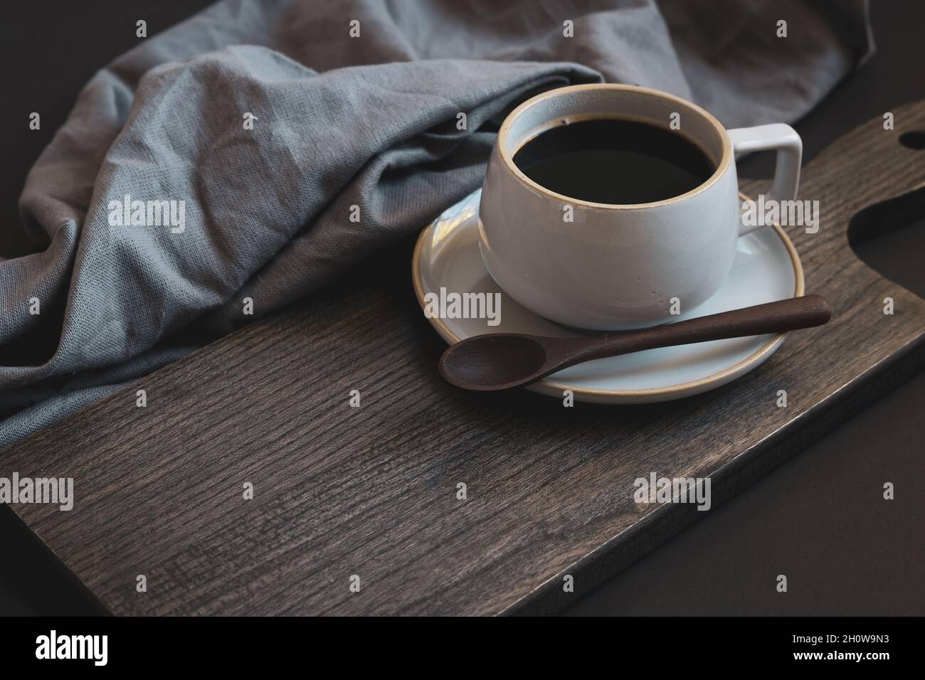 Semplice tazza di caffè su un piattino con un piccolo cucchiaio di legno e lino grigio su sfondo nero con spazio di copia Foto Stock