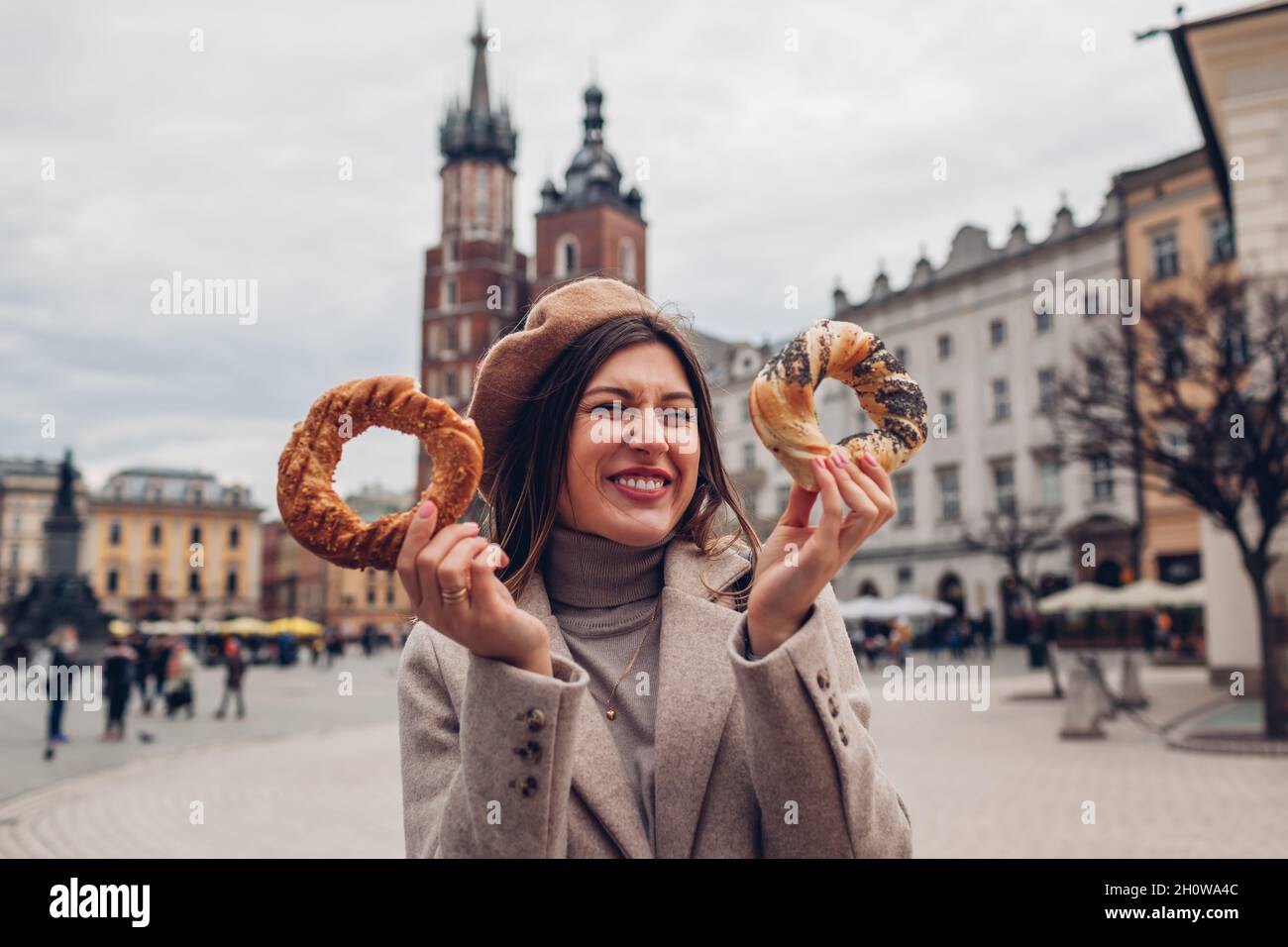 Donna turistica che mangia bagel obwarzanek cucina tradizionale polacco snack waling sulla piazza del mercato di Cracovia. Viaggiare in Europa in autunno Foto Stock