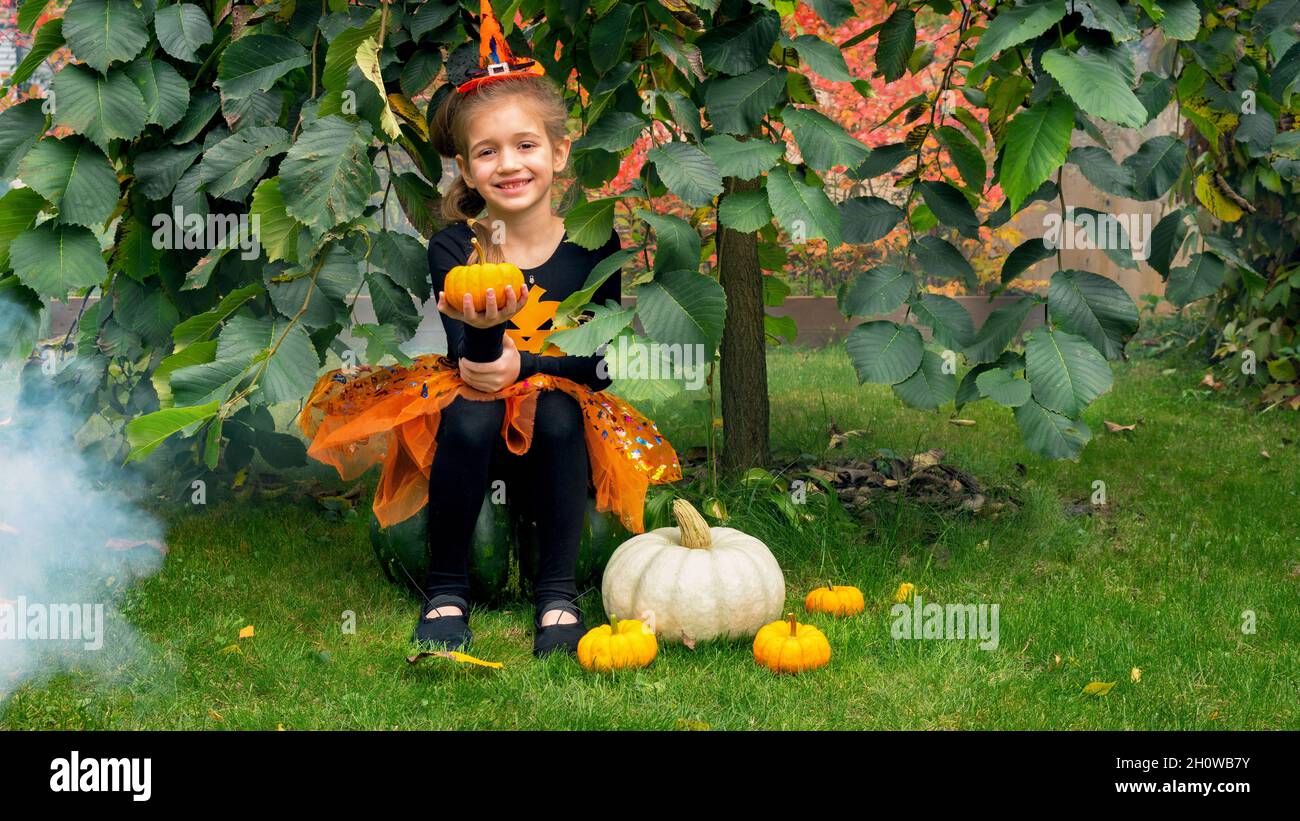 La piccola strega si siede su una zucca in un giardino d'autunno. Una ragazza vestita come strega per Halloween. I bambini festeggiano Halloween in abiti da carnevale. Tre Foto Stock