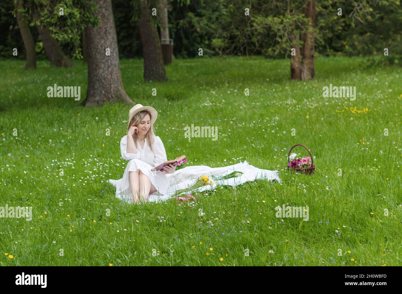 Una ragazza sorridente che legge un libro su una coperta nella foresta. Foto Stock