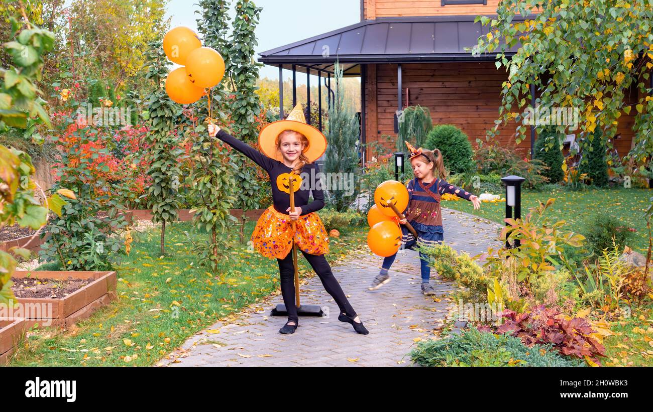 I bambini giocano le streghe sui broomsticks su Halloween. Le streghe di Halloween volano sulle scopa. Ragazze felici con palloncini corrono lungo i sentieri del giardino. Bambini Foto Stock