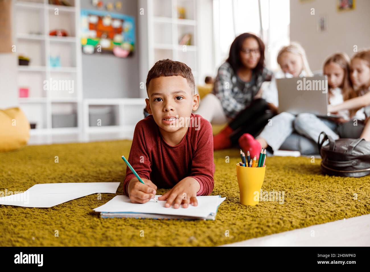 Sorridendo ragazzino che tiene una matita e che disegnava su carta sul pavimento Foto Stock