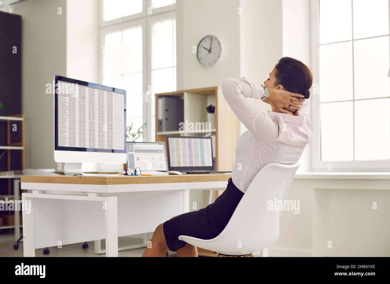 Un dipendente felice si rilassa mentre si siede alla sua scrivania con i computer in ufficio Foto Stock