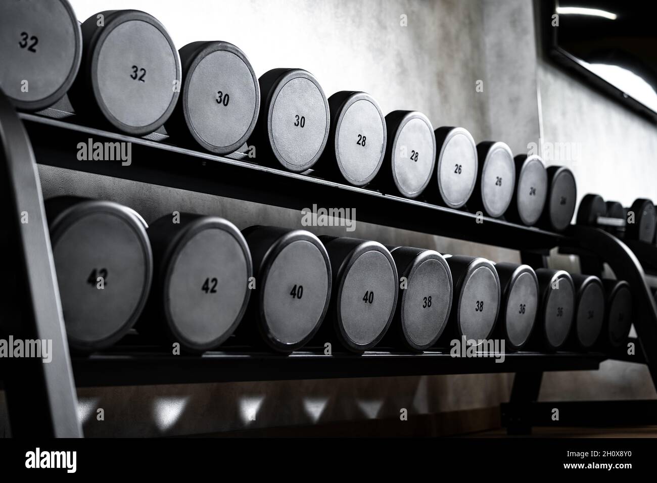 File di manubri in metallo su rack per bodybuilding in palestra Foto Stock