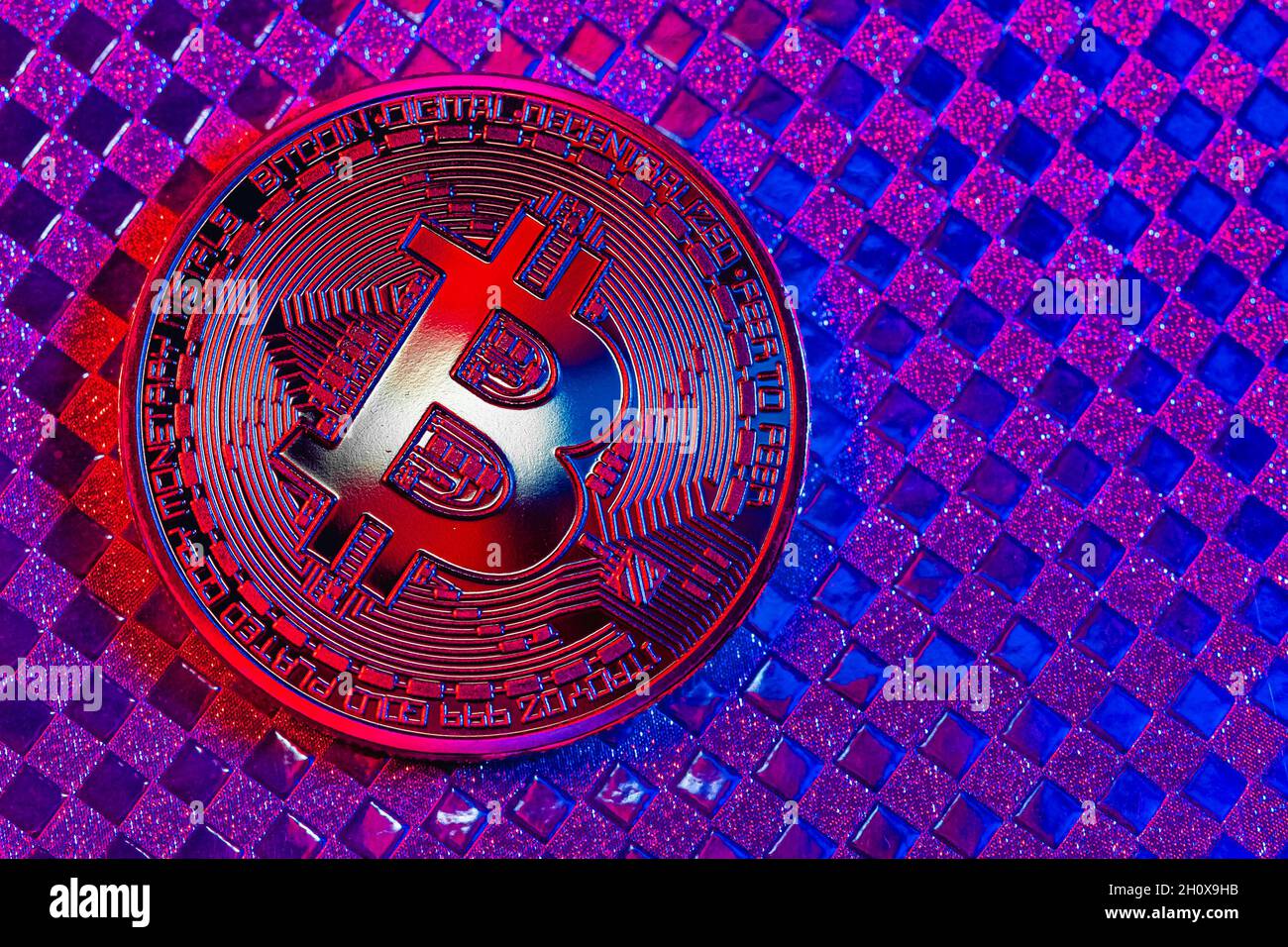 Bitcoin d'oro in una luce mista blu e rossa su uno sfondo colorato Foto Stock