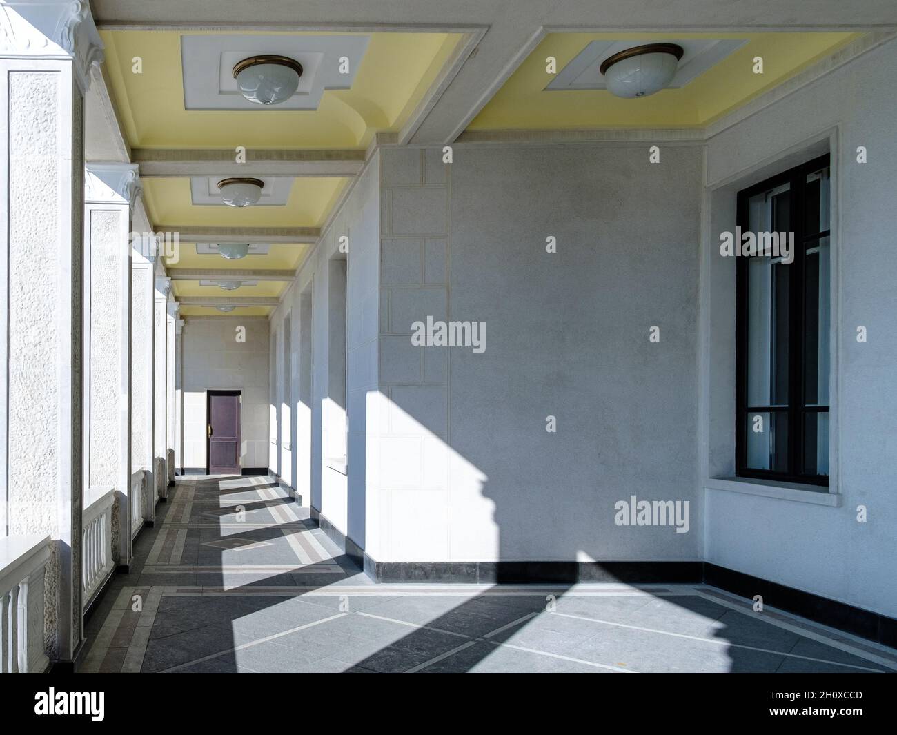 Vista delle colonne della galleria in un edificio sconosciuto. La luce solare brillante attraverso le colonne crea un motivo geometrico di luce e ombra sul pavimento e sulle pareti. Foto Stock