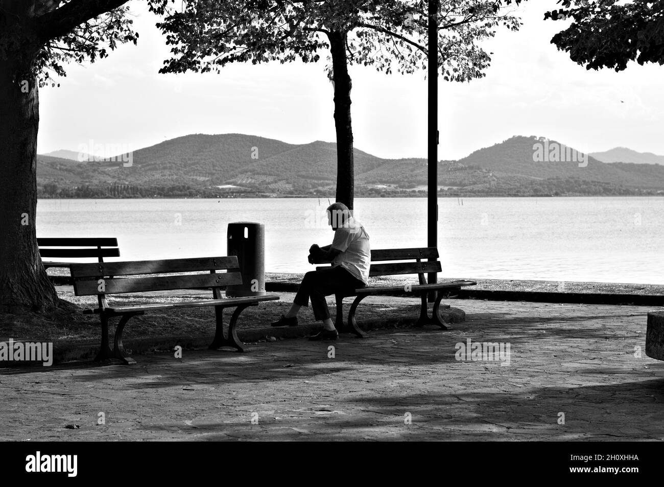 La solitudine di un uomo isolato seduto sulla panchina di fronte al Lago Trasimeno (Umbria, Italia, Europa) Foto Stock