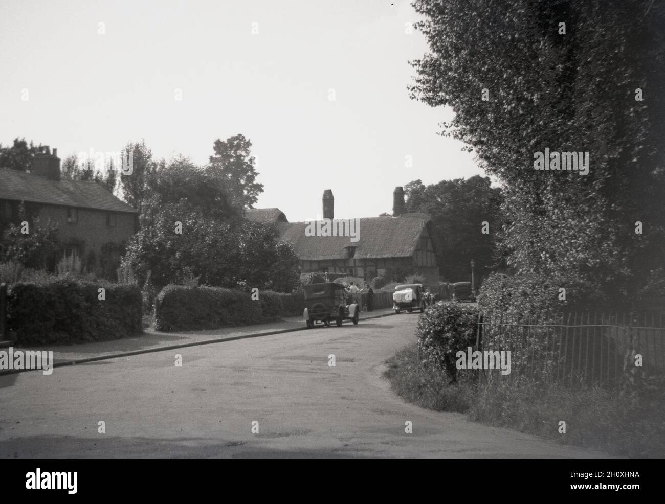 1940, immagine storica che mostra le automobili dell'epoca parcheggiate in una tranquilla strada di campagna accanto al cottage di Anne Hathaway, Stratford-upon-Avon, Inghilterra, Regno Unito. Questa fattoria con tetto in paglia, vista in lontananza, era la casa d'infanzia della moglie del famoso drammaturgo inglese William Shakespare e si trova a Shottery appena fuori Stratford. Fu la casa della famiglia Hathaway per 400 anni, fino al 1911. Foto Stock