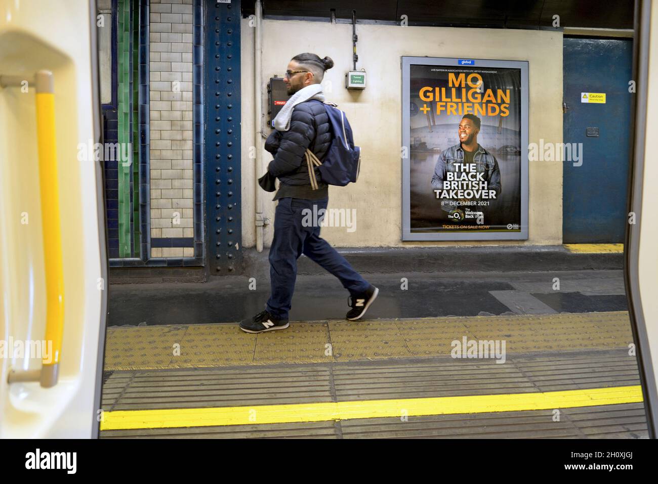 Londra, Inghilterra, Regno Unito. Metropolitana di Londra: L'uomo passa accanto al poster di Mo Gilligan nella stazione della metropolitana di St James's Park Foto Stock