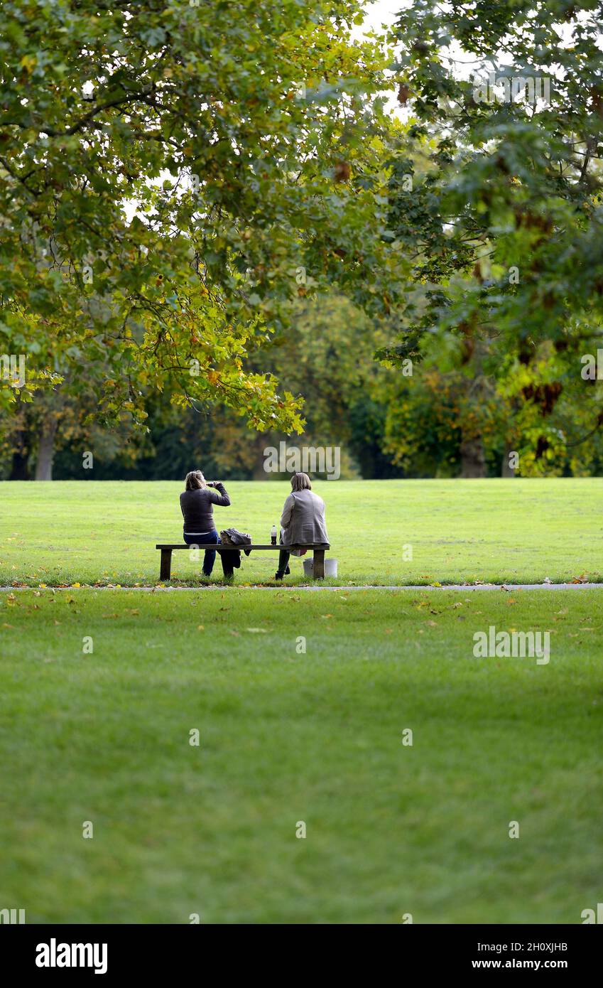 Londra, Inghilterra, Regno Unito. Regent's Park: Due donne che parlano su una panca, una che beve (Diet Coca Cola) Foto Stock
