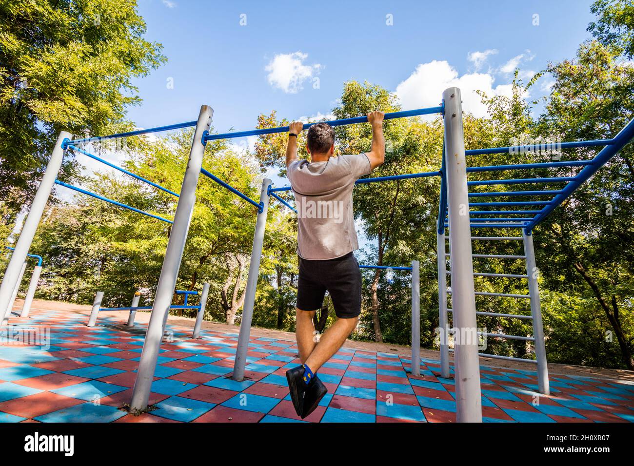Un uomo che fa esercizi su una barra orizzontale in un parco. Sport all'aperto. Foto Stock