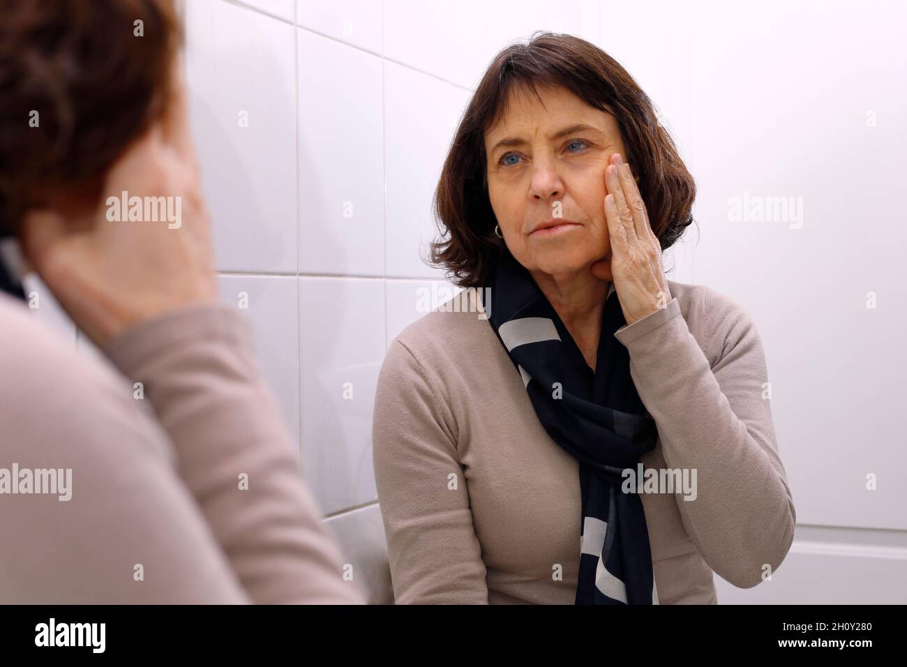 Una donna matura che guarda nello specchio il suo volto Foto Stock
