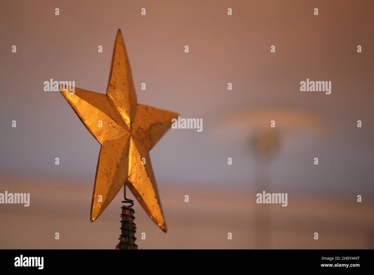 Primo piano di un'enorme stella dorata come un topper dell'albero di Natale con alcuni rami superiori dell'albero. Luce calda e accogliente. Allegra e felice immagine a colori. Foto Stock