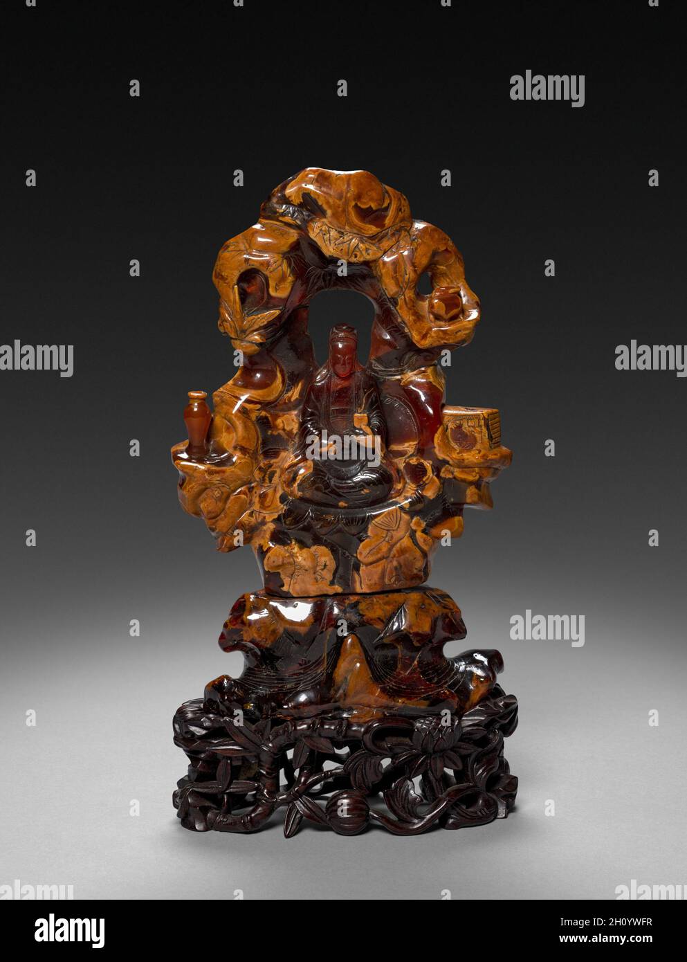 Bodhisattva Guanyin seduto in una roccia Grove, 1675-1700. Cina, dinastia Qing (1644-1911). Ocra opaco e traslucido rosso-arancione ambra; complessivo: 22,9 cm (9 in.). Foto Stock