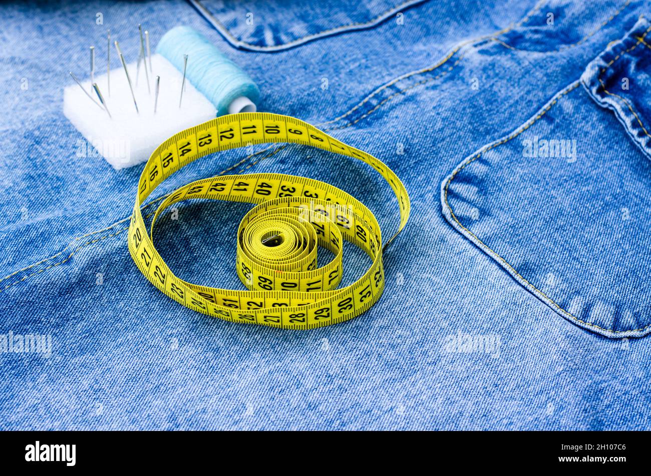 Ci sono articoli da cucire sopra gli articoli di denim. Un centimetro, fili, perni e un ditale si trovano sulle cose. Concetto di taglio e cucitura. Foto Stock