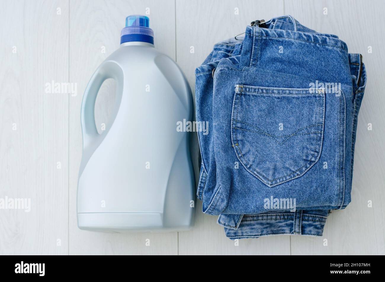 Grande bottiglia di plastica di polvere liquida e una pila di articoli di denim sulla vista del piano d'esame. Detergenti e prodotti per la pulizia. Foto Stock