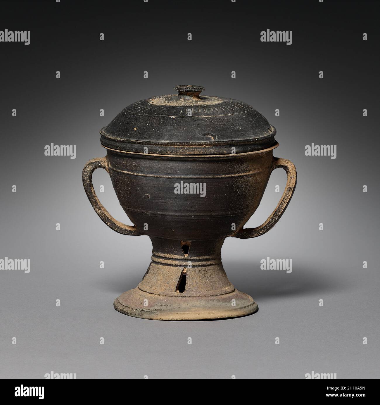 Tazza con coperchio e manici a tracolla, ad 300s-400s. Corea, periodo Kaya (ad 42-562). Gres con smalto in frassino naturale; lunghezza complessiva: 21.1 cm (8 5/16 in.); diametro esterno: 15.7 cm (6 3/16 in.). Vasi di ceramica con un basamento del piede come questo è il primo high-fired ware conosciuto. Il suo colore grigio è il risultato della riduzione dell'ossigeno nella camera chiusa del forno. Le imbarcazioni a piedi non erano per uso quotidiano, ma servivano piuttosto a presentare offerte al defunto. Foto Stock