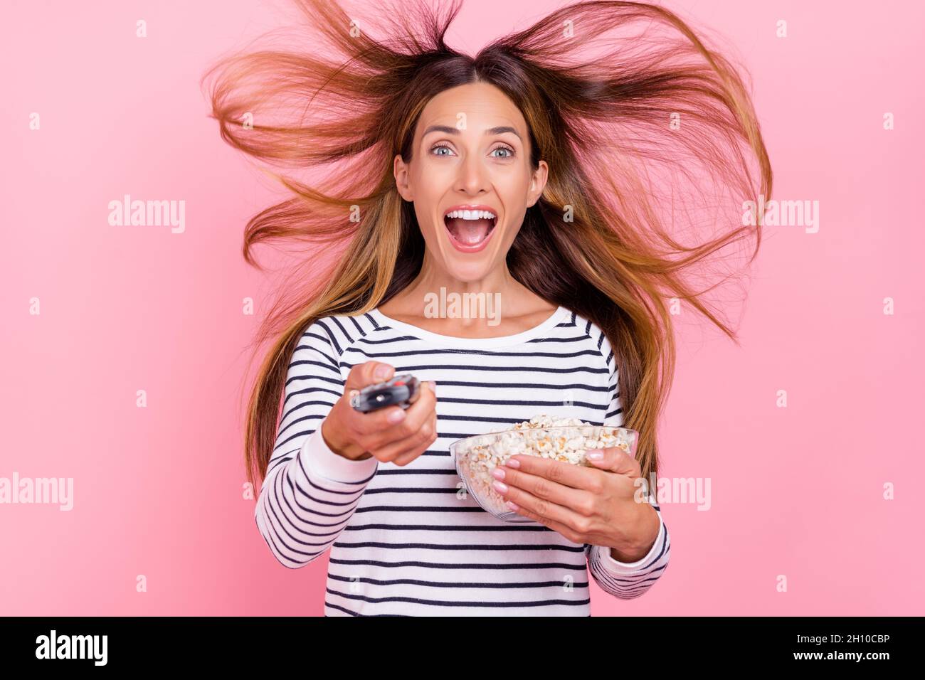 Foto di funky scioccato donna matura indossare a strisce maglione sorridente ala soffiando guardare la tv mangiare popcorn isolato colore rosa sfondo Foto Stock