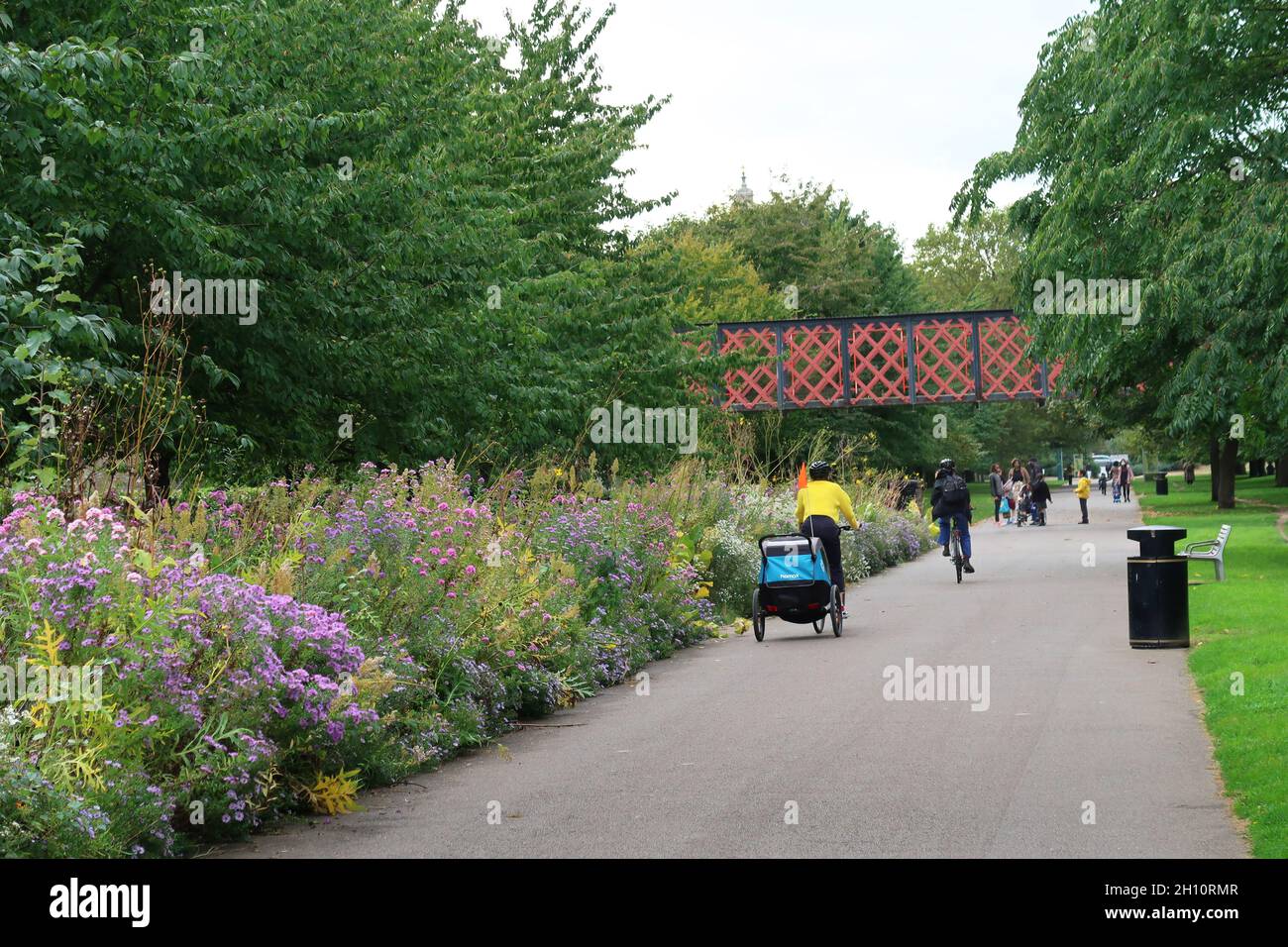 Burgess Park, Peckham, Londra, Regno Unito. Un ciclista con un rimorchio per biciclette per bambini utilizza il percorso che segue il vecchio canale di Surrey. Foto Stock