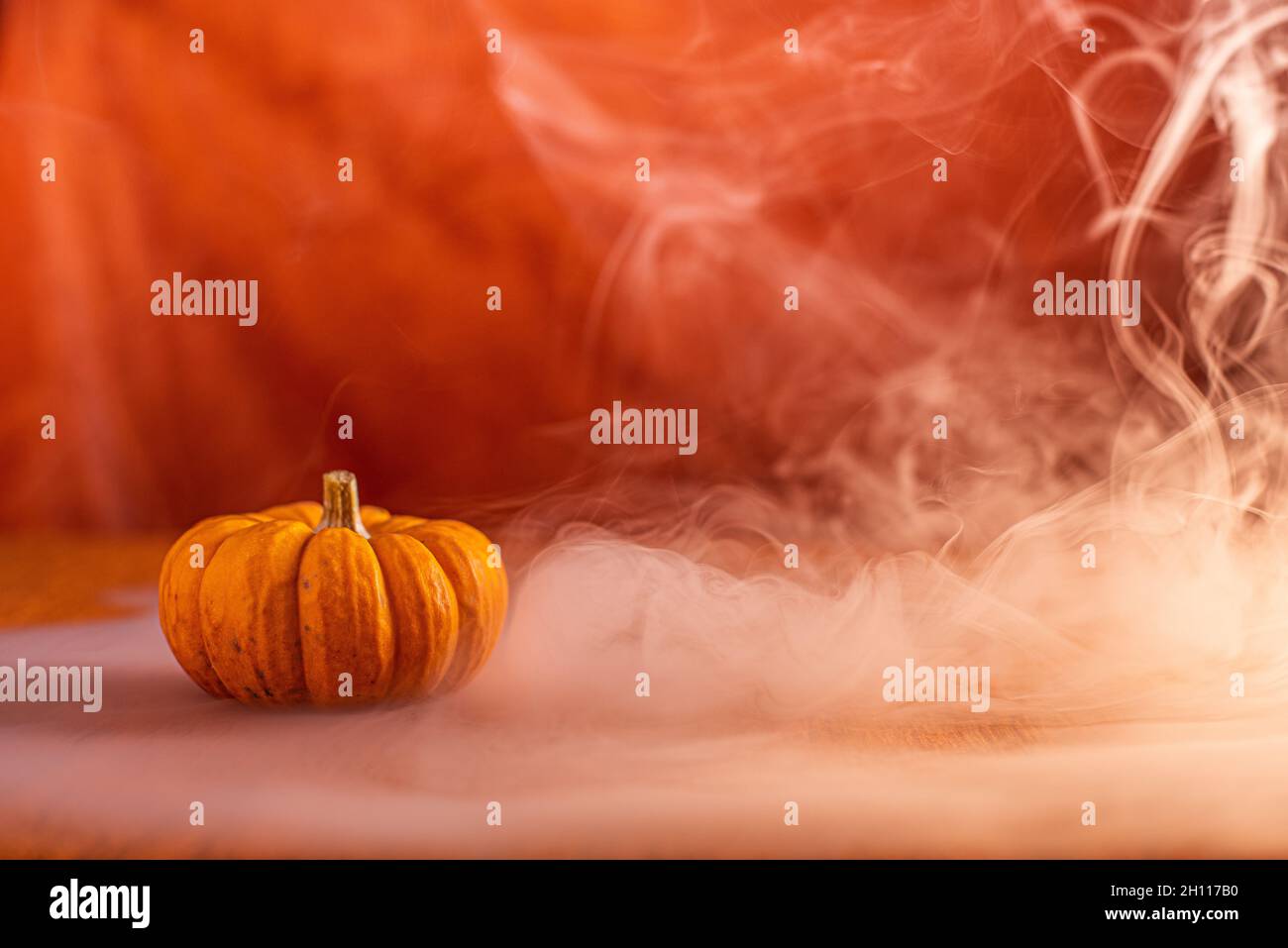 La zucca di Halloween si trova sul tavolo, lo sfondo arancione, c'è fumo tutto intorno Foto Stock