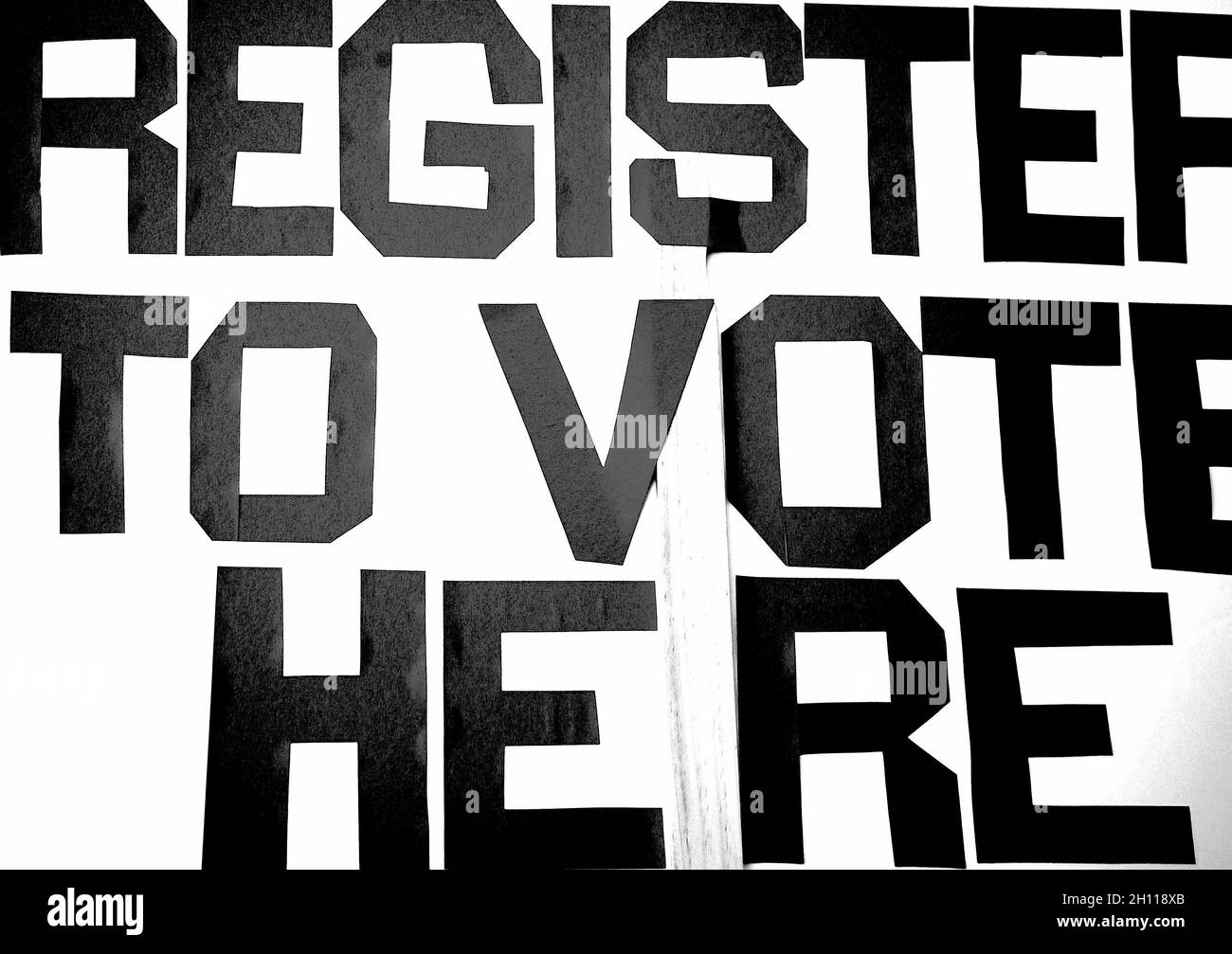 Primo piano di un cartello con un testo ''Registrati qui'' scritto in nero su sfondo bianco Foto Stock