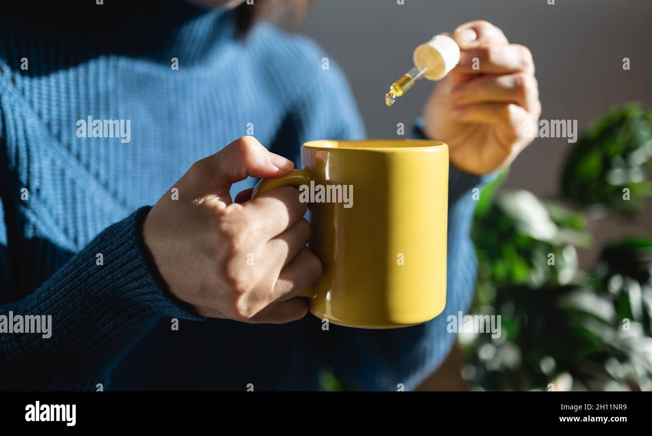 CBD olio di canapa - Donna che prende l'olio di cannabis in tazza di tè per il trattamento di ansia - Focus sulla mano sinistra Foto Stock
