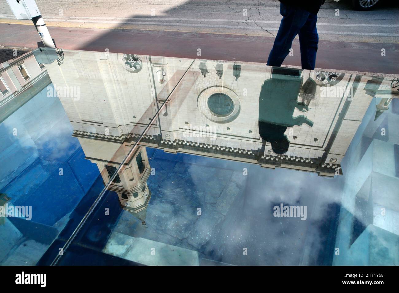 Pescara, Abruzzo, Italia. Un pedone passa davanti a un'area panoramica in vetro che mostra la base di una colonna storica fuori dalla Cattedrale di San Cetteo. Foto Stock