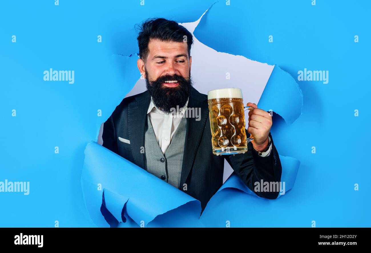 Uomo bearded con la tazza di birra che guarda attraverso il foro di carta. Pubblicità Oktoberfest. Bevande, alcolici e concetto di tempo libero Foto Stock