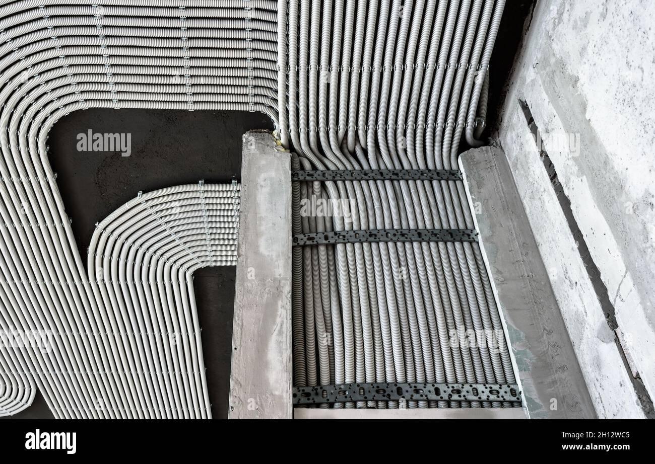 Cavi e tubi elettrici su pareti e soffitti in calcestruzzo. Tubi flessibili e condotti in plastica moderni con fili in camera. Linee dei tubi di cablaggio in pvc dopo Foto Stock