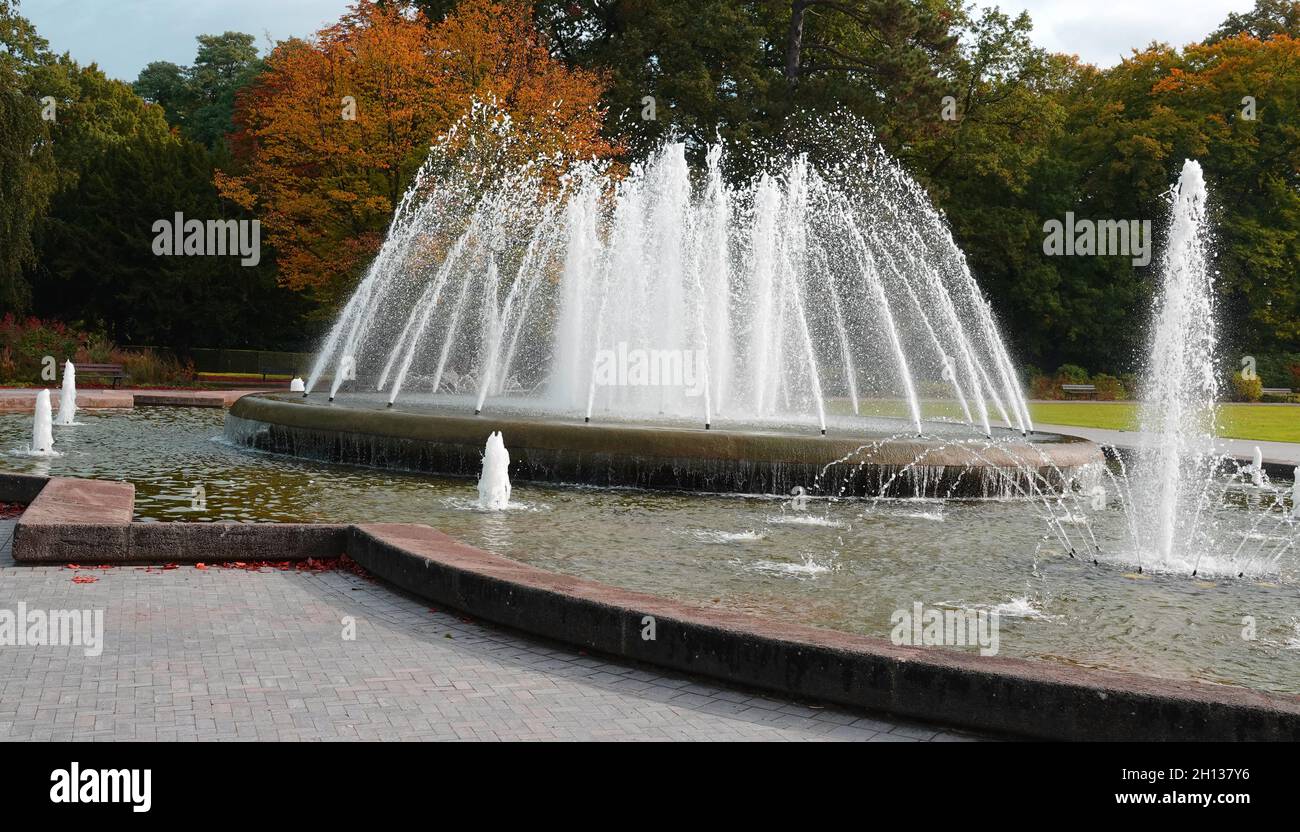 I giardini termali di Bad Oeynhausen, in Germania, hanno una grande fontana nel mezzo. Sullo sfondo gli alberi che iniziano ad ottenere i loro colori autunnali. Foto Stock