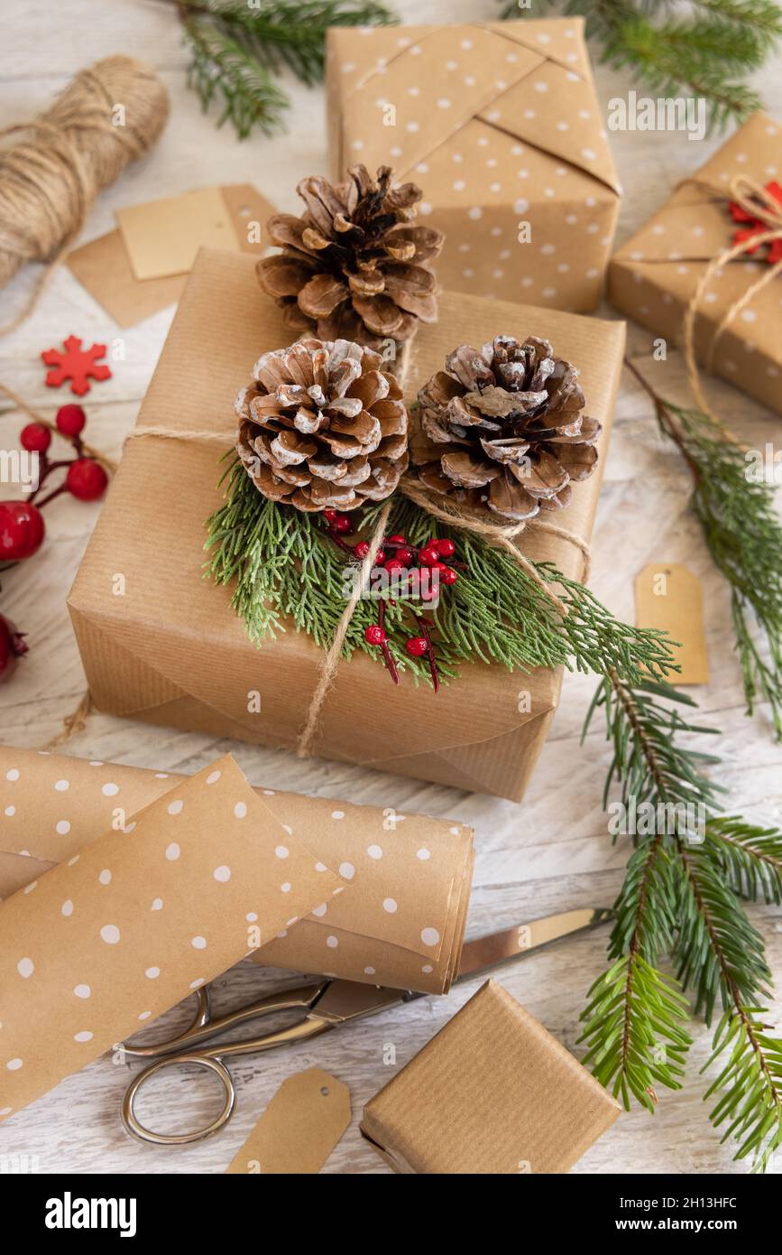 Regalo di Natale avvolto decorato con coni di pino e rami di ginepro su sfondo bianco da vicino. Spazio di copia Foto Stock