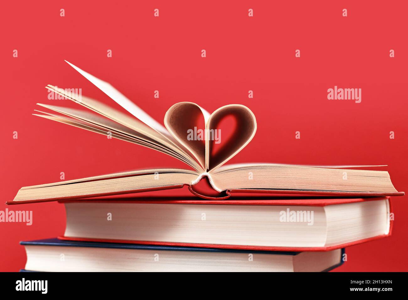 Pagine piegate a forma di cuore su una pila di vecchi libri di copertina rigida su sfondo rosso Foto Stock