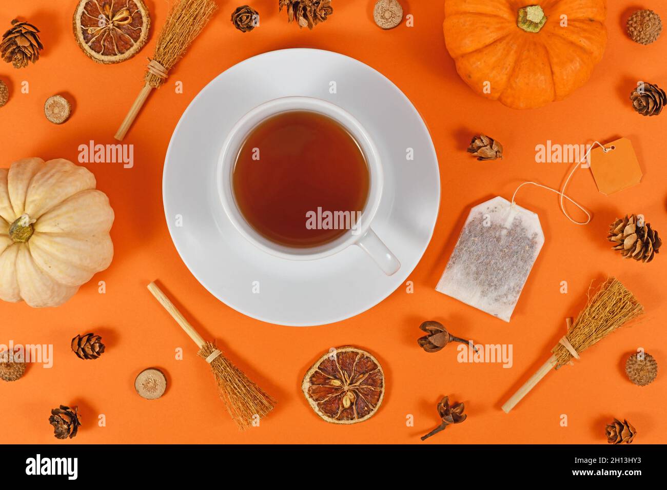 Tazza di tè circondata da decorazioni autunnali stagionali come zucche e fette d'arancia su sfondo arancione Foto Stock