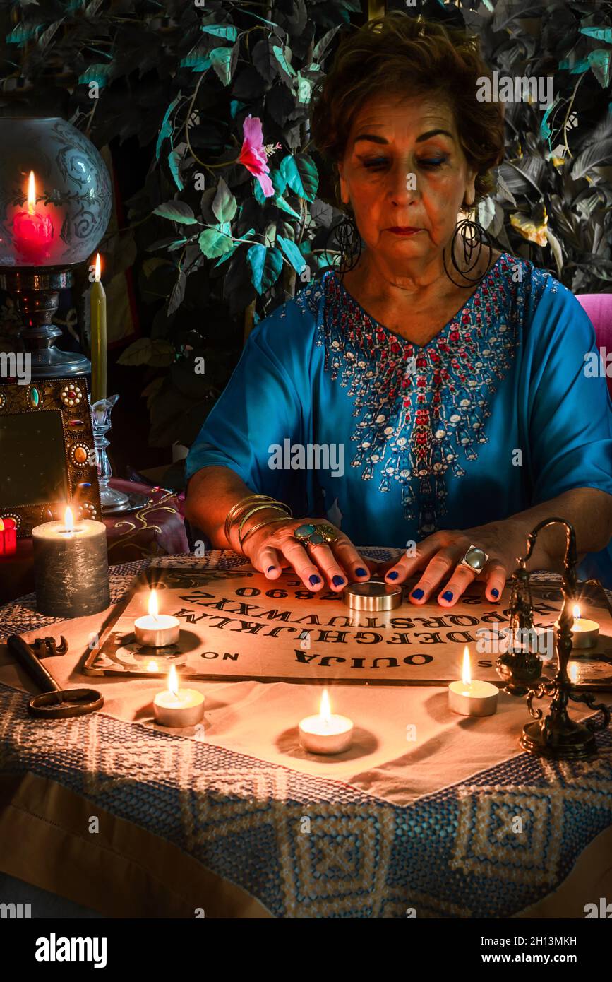 Donna Pythoness che esegue un seance su una scheda Ouija con molte candele accese. Halloween idee Foto Stock