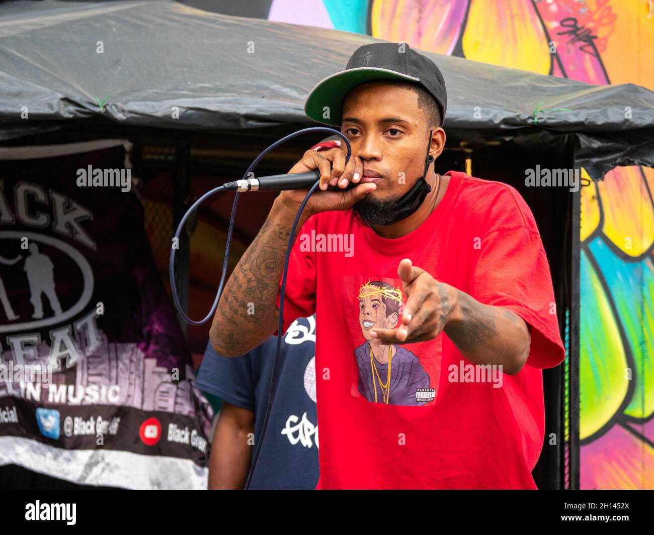 Medellin, Antioquia, Colombia - 6 gennaio 2021: Giovane uomo latino con capelli ricci canta Hip-Hop con microfono nero contro Muro colorato Foto Stock