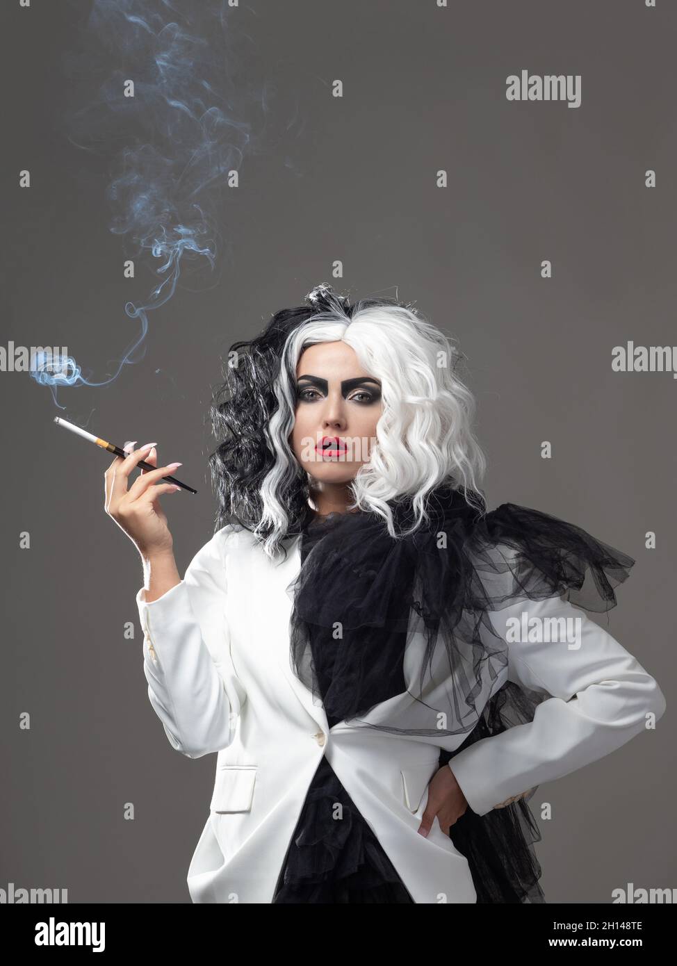 Una donna carismatica insolita in un abito bianco e nero con capelli bianchi e neri fuma una sigaretta utilizzando un boccaglio, un'immagine audace ed elegante di un Foto Stock
