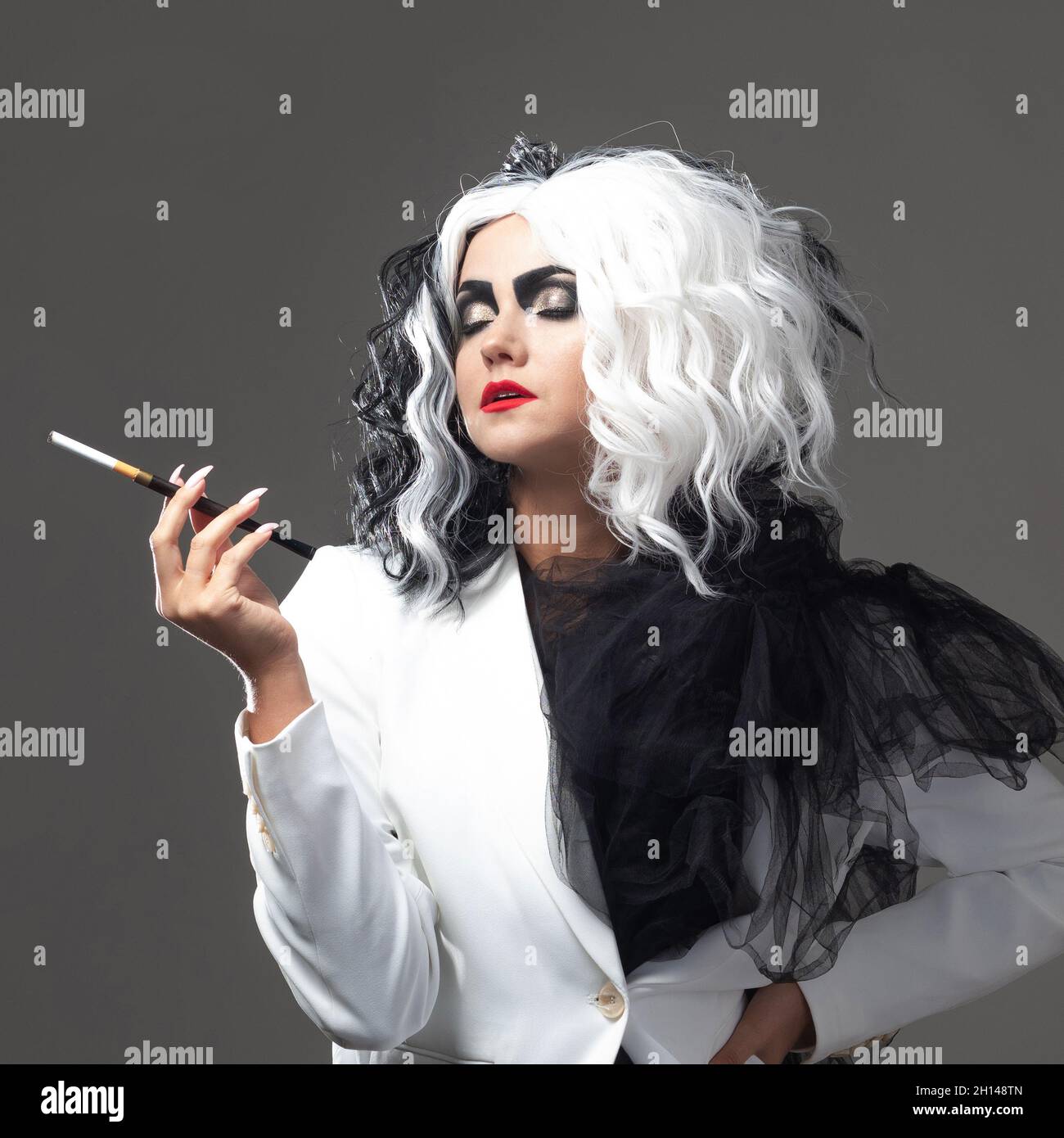 Una donna carismatica insolita in un abito bianco e nero con capelli bianchi e neri fuma una sigaretta utilizzando un boccaglio, un'immagine audace ed elegante di un Foto Stock