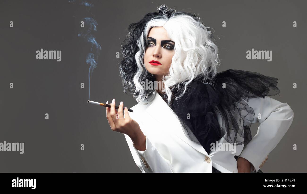 Una donna carismatica insolita in un abito bianco e nero con capelli bianchi e neri fuma una sigaretta utilizzando un boccaglio, un'immagine audace ed elegante di un Foto Stock