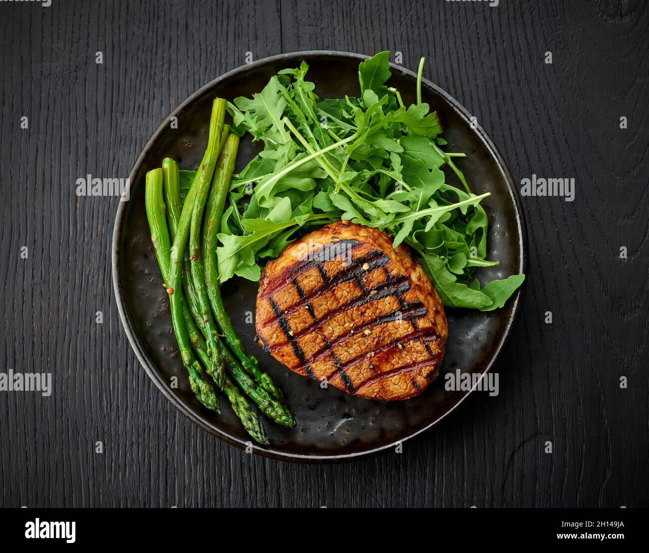 Bistecca di vitello appena cotta, asparagi e rucola serviti su piatto scuro, vista dall'alto Foto Stock