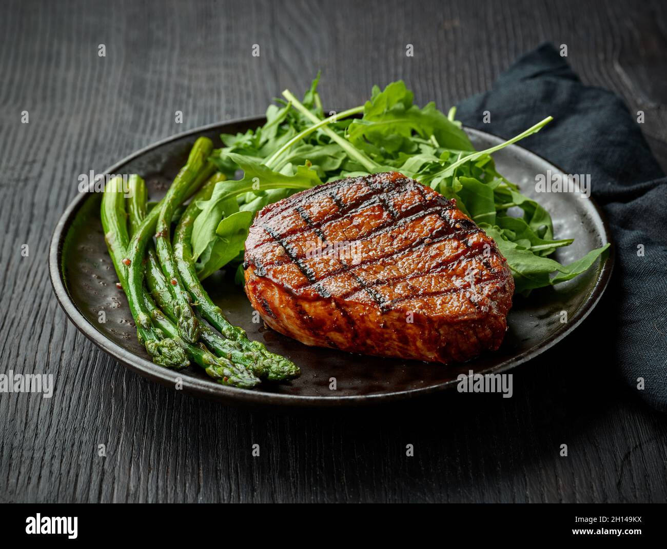 Bistecca di vitello appena cotta, asparagi e rucola serviti su piatto scuro Foto Stock