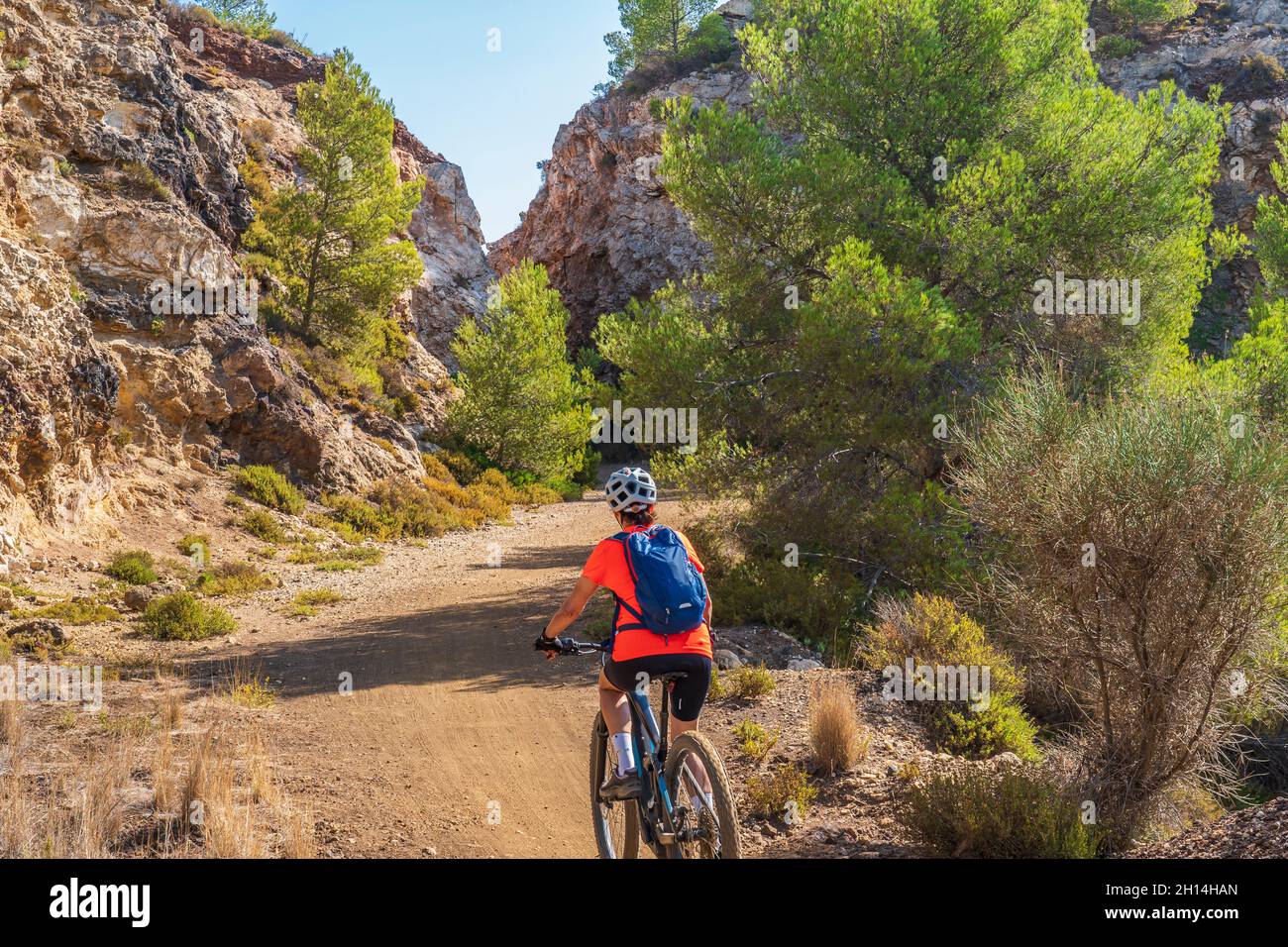 Bella donna che guida la sua mountain bike elettrica sulla costa del mediterraneo, sull'Isola d'Elba, nell'Arcipelago toscano, di fronte a Porto Foto Stock