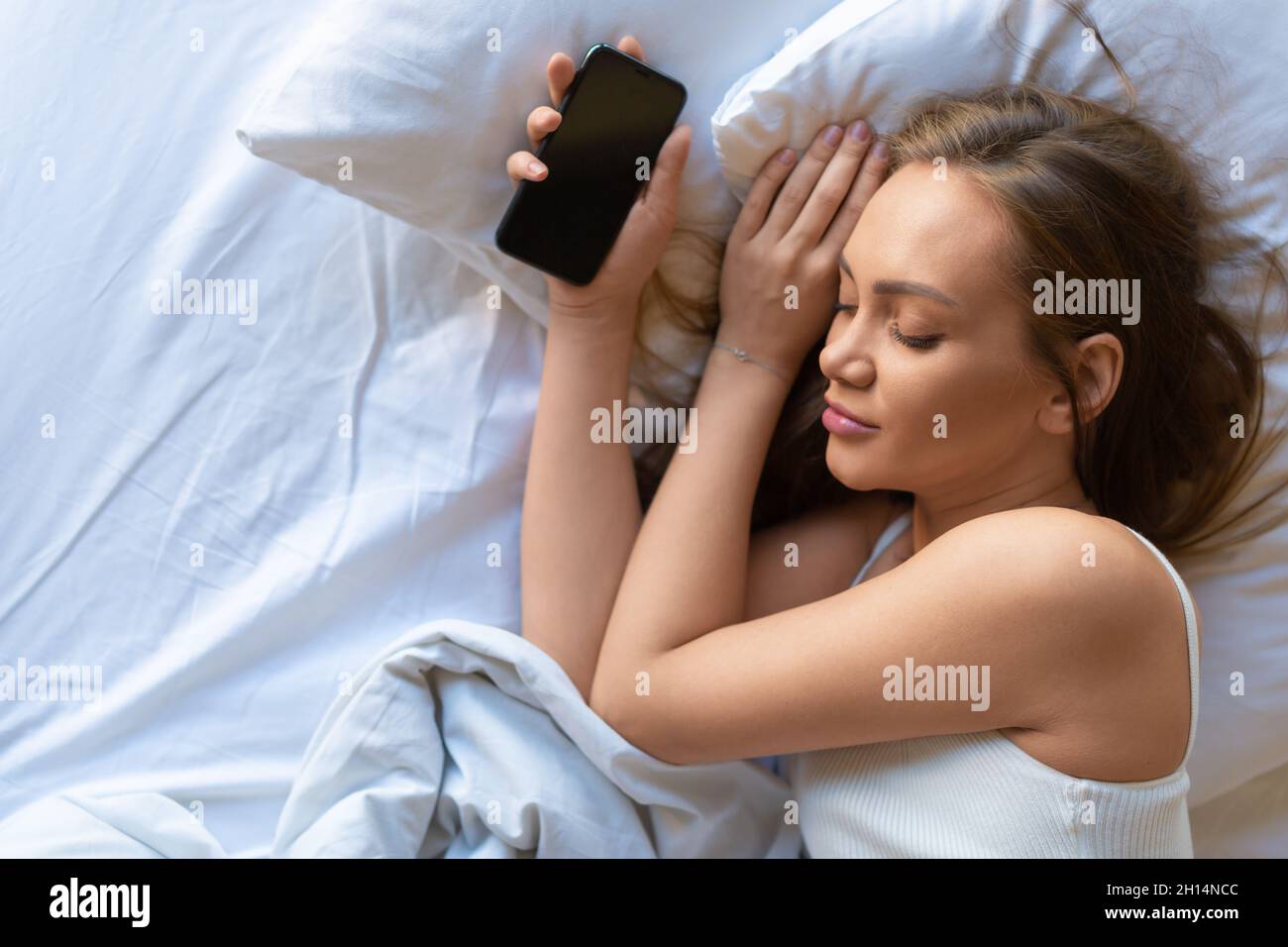 Foto di una donna a letto con uno smartphone. Concetto di aggiunta dei social network. Vista dall'alto. Foto Stock