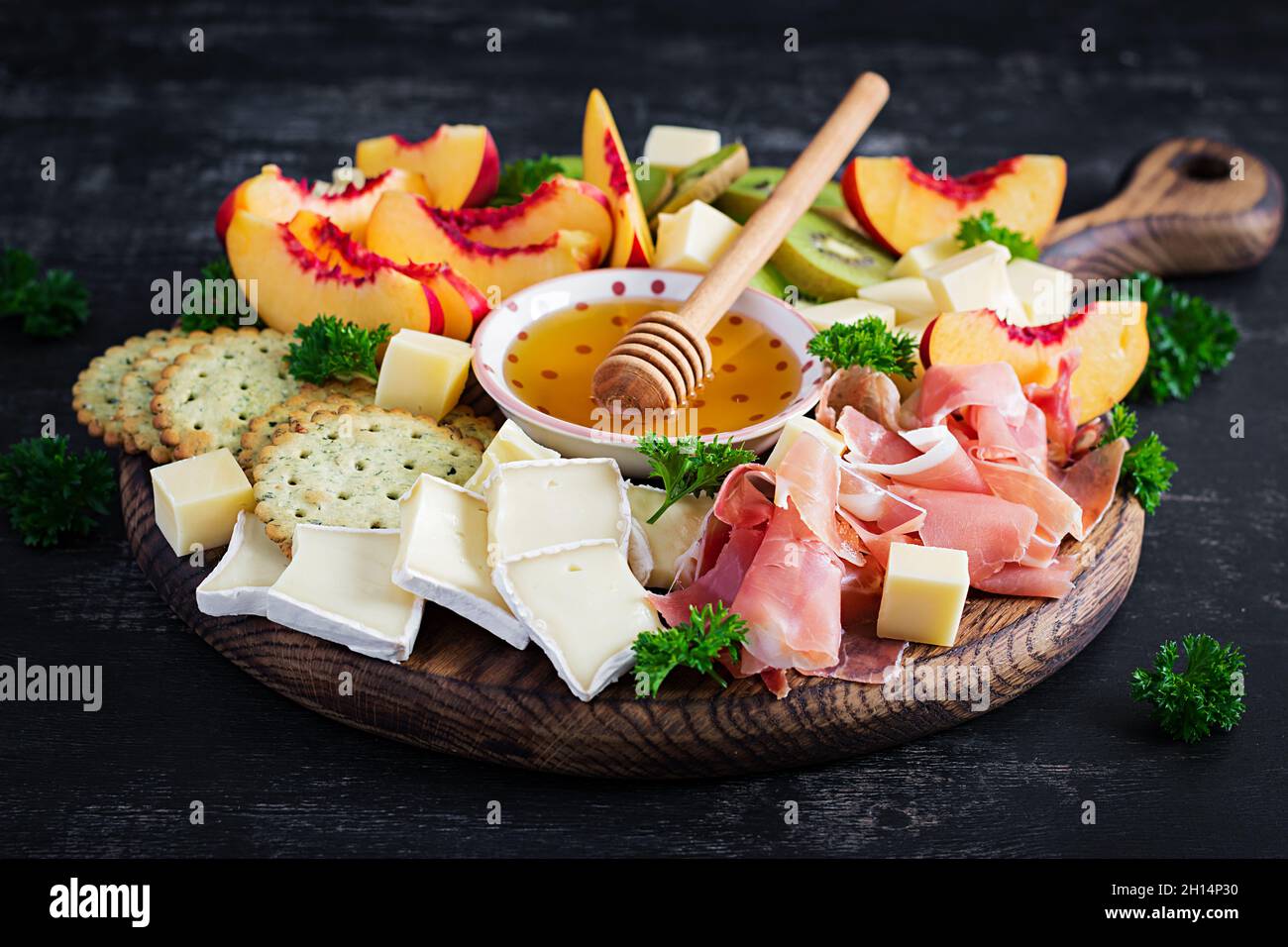 Piatto di antipasti italiani con prosciutto, formaggio e frutta su sfondo scuro. Foto Stock