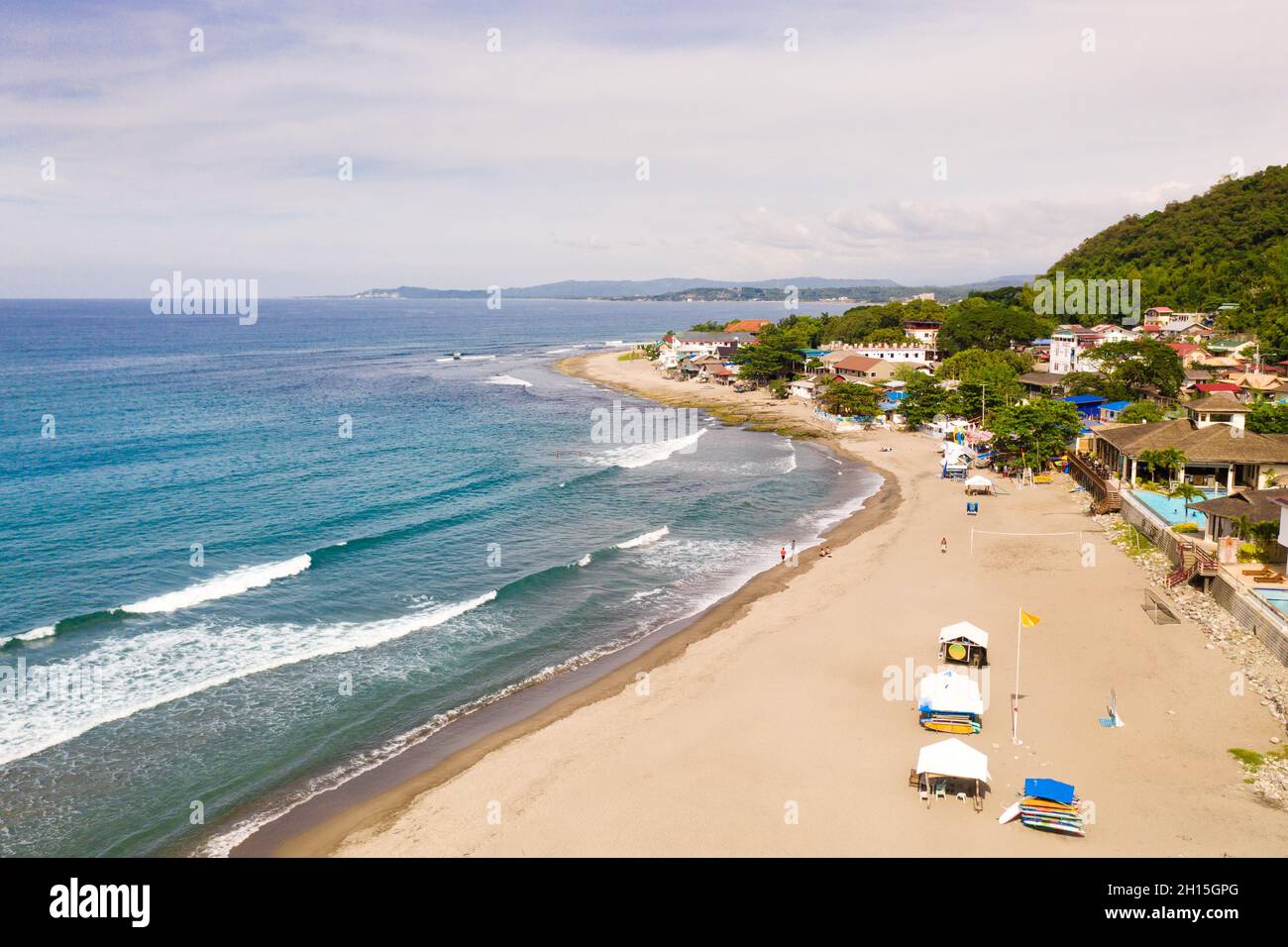 Costa sabbiosa, edifici e mare blu con onde. San Juan, la Union, Filippine. Città costiera con una spiaggia di surfisti. Le spiagge dell'Islan filippino Foto Stock