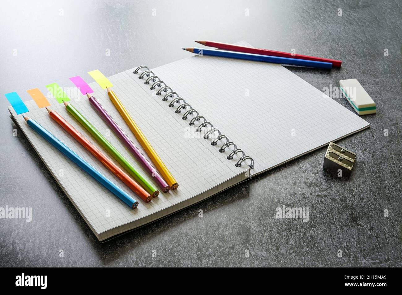 Scrivania creativa con notebook a spirale, matite colorate e materiali di consumo su una superficie grigia, spazio di copia, messa a fuoco selezionata, profondità di campo ridotta Foto Stock